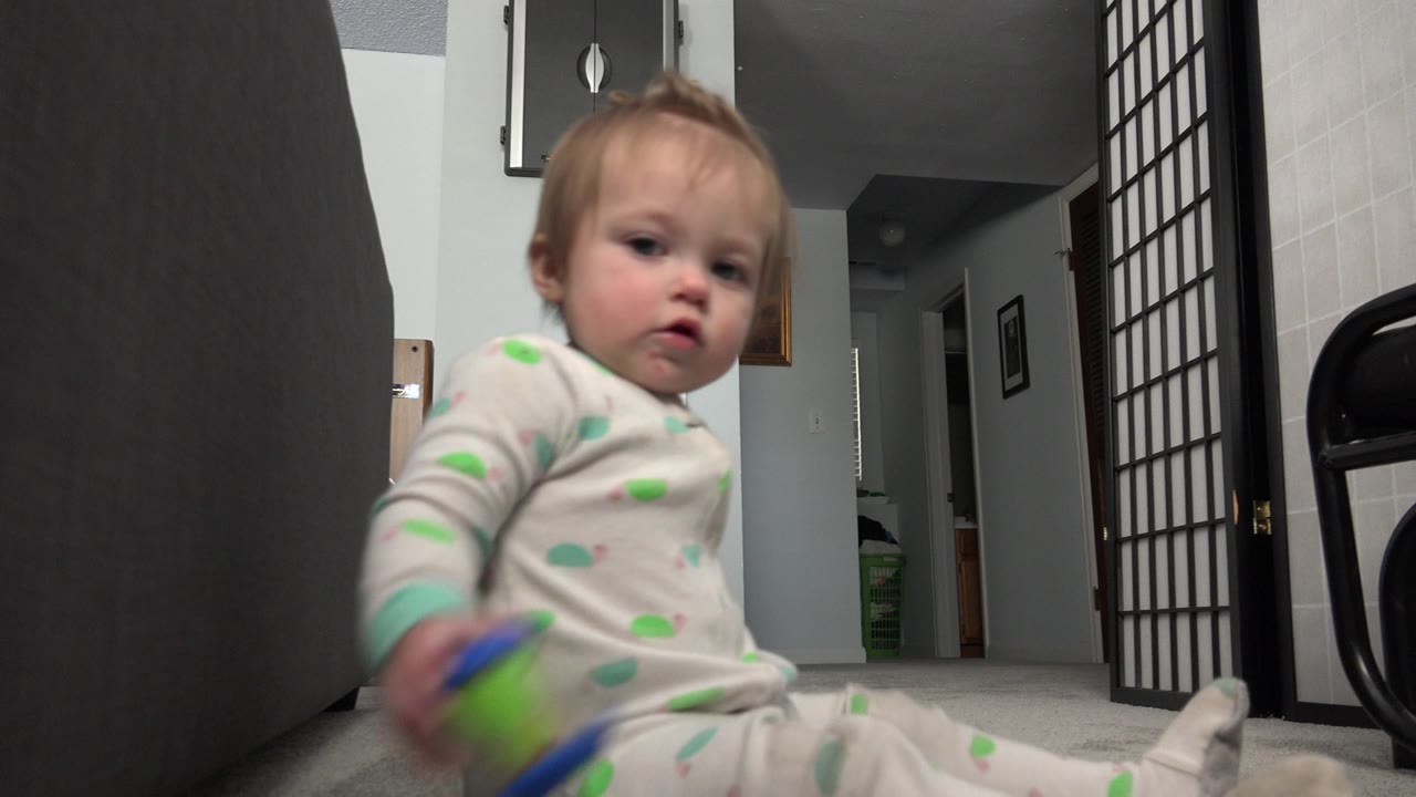 The toddler remains close to the low camera in the Westminster, Colorado home, with the colorful toy blurred by movement near the foreground.