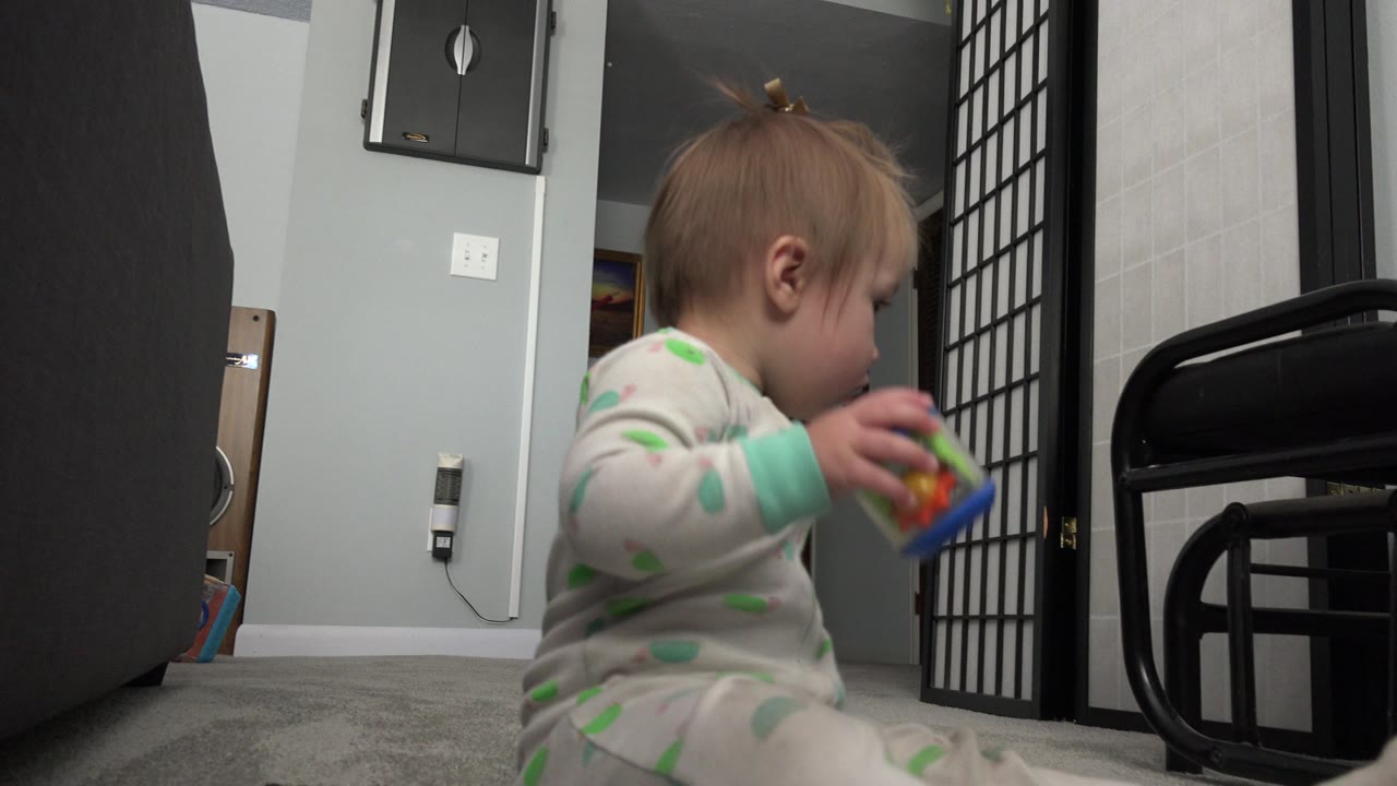Toddler sitting on carpet holding a colorful toy indoors.
