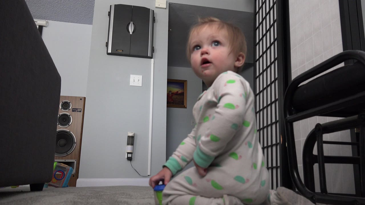A young boy in spotted pajamas sits on a carpeted floor in a Westminster, Colorado home interior, looking upward beside dark furniture and a wall speaker.