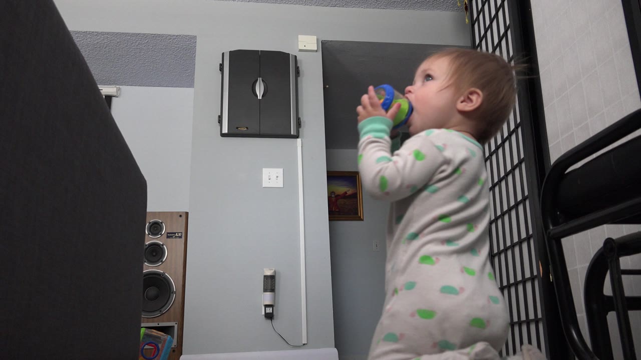 Infant in a patterned sleeper chewing a blue and green object indoors.