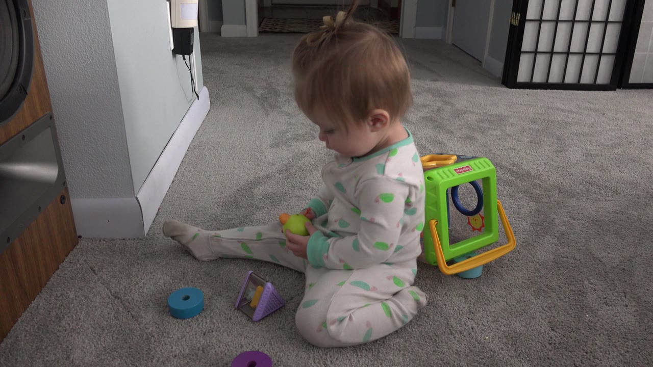 Baby sitting on carpet beside colorful toys in a home interior.