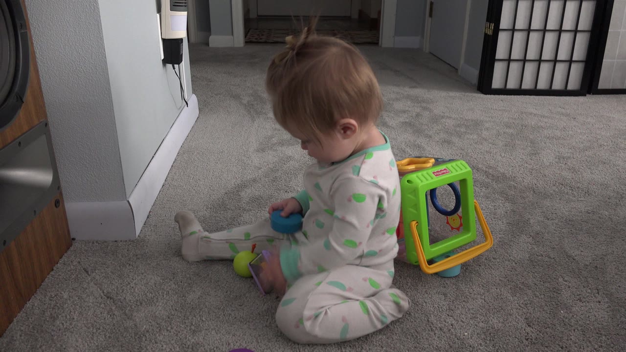 Toddler seated on carpet with colorful toys nearby.