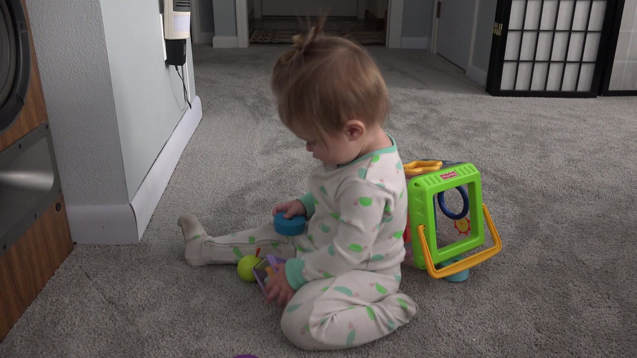 The child looks down toward toys on the gray carpet in the Westminster home, with the bright green activity cube still visible behind her.