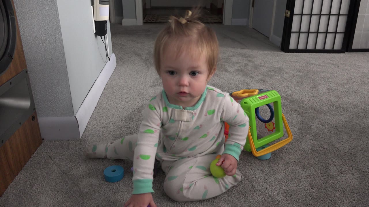 Young child sitting on gray carpet beside colorful toys.