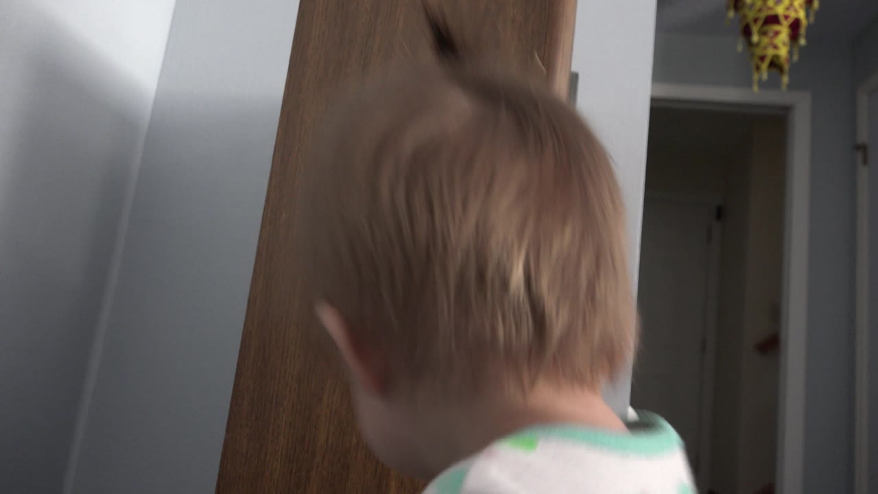 The toddler's head and shoulders fill the lower frame near the wood speaker, with a dark doorway and indoor walls visible in the Westminster, Colorado home.