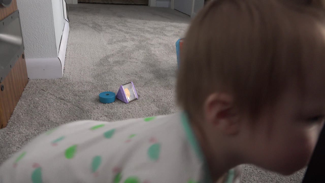 Toddler close to the camera on gray carpet with small toys in the room.