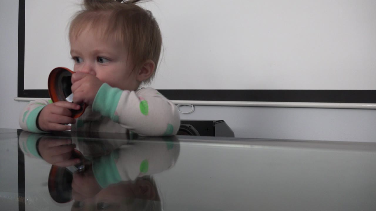 Toddler chewing a small bell at a glass table.