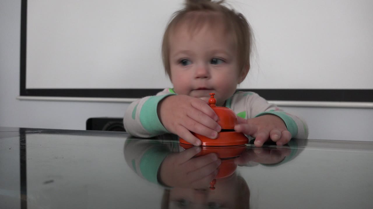 Young child behind a glass table holding an orange object.