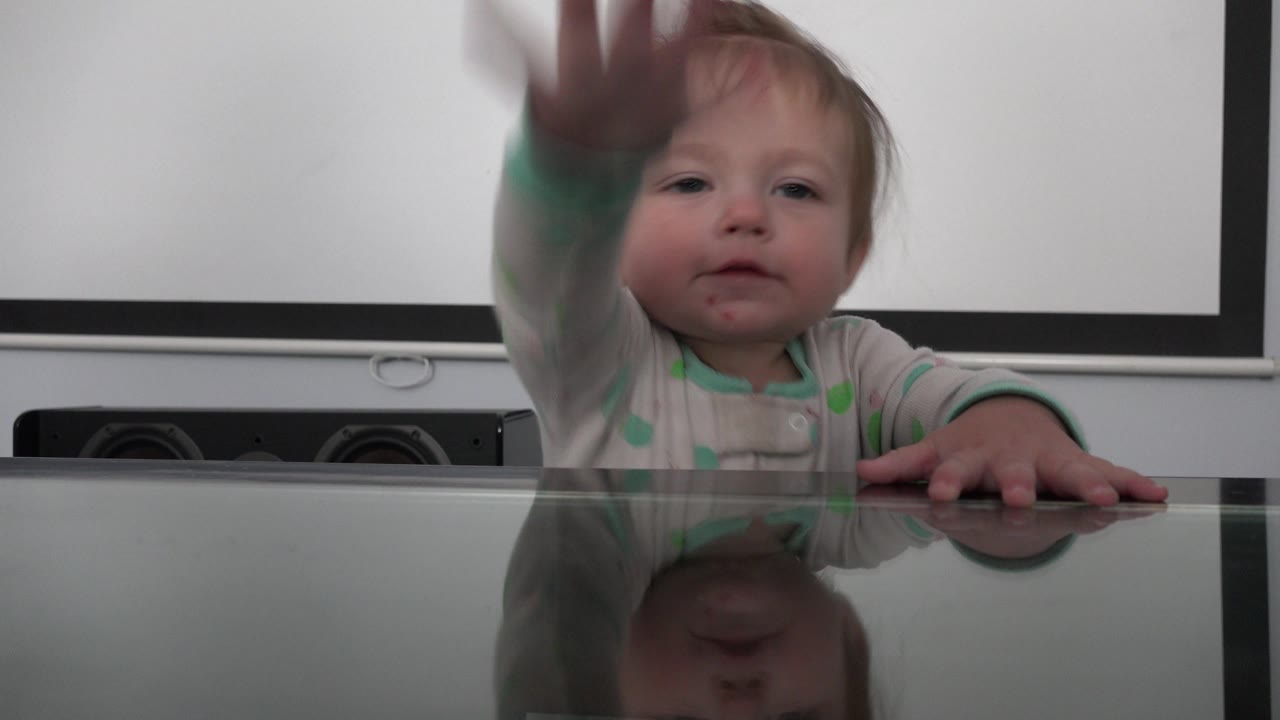 Baby raises a hand toward the camera above the table.
