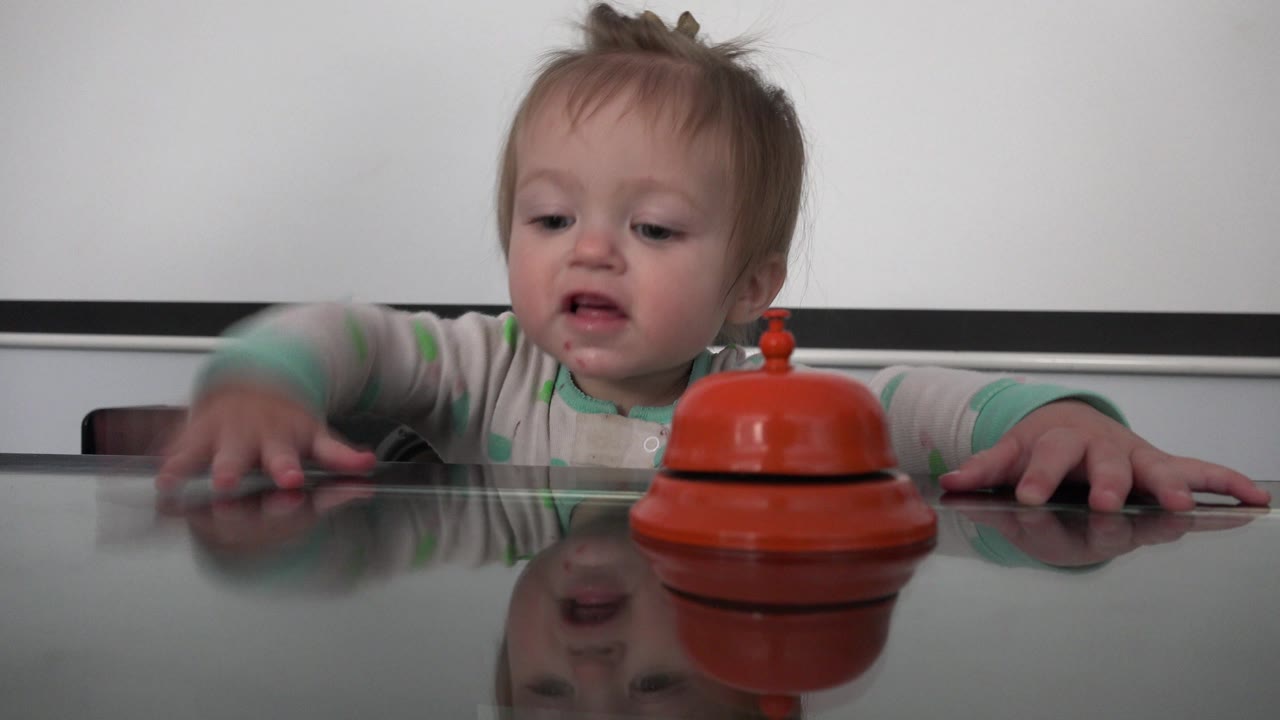 At 0:01 in Westminster, Colorado, the child leans forward with one hand blurred in motion toward the orange bell on the reflective table.