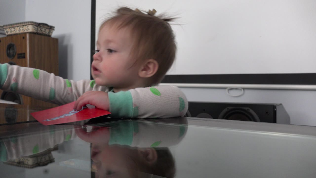 Toddler reaching across a glass table with a red paper item.