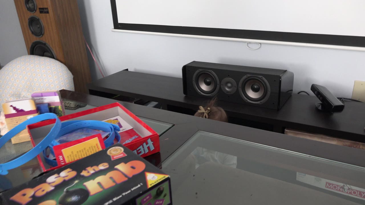 Glass table with game boxes, blue toy track, speakers, and a baby partly visible behind the table.