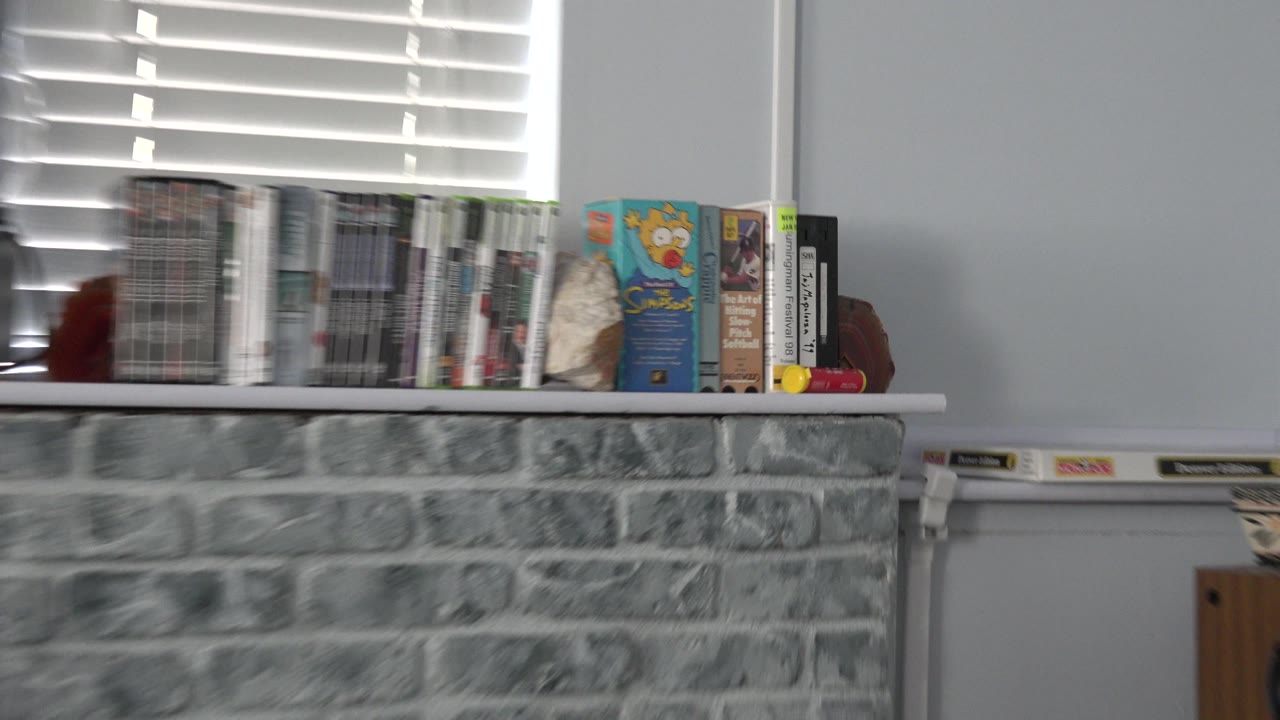 DVDs and VHS tapes on a mantel above a gray stone fireplace