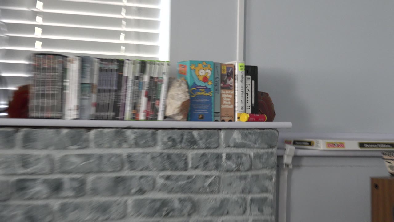 The Westminster home clip continues across a row of media cases on a white mantel, with bright horizontal blinds behind the shelf and no visible people.