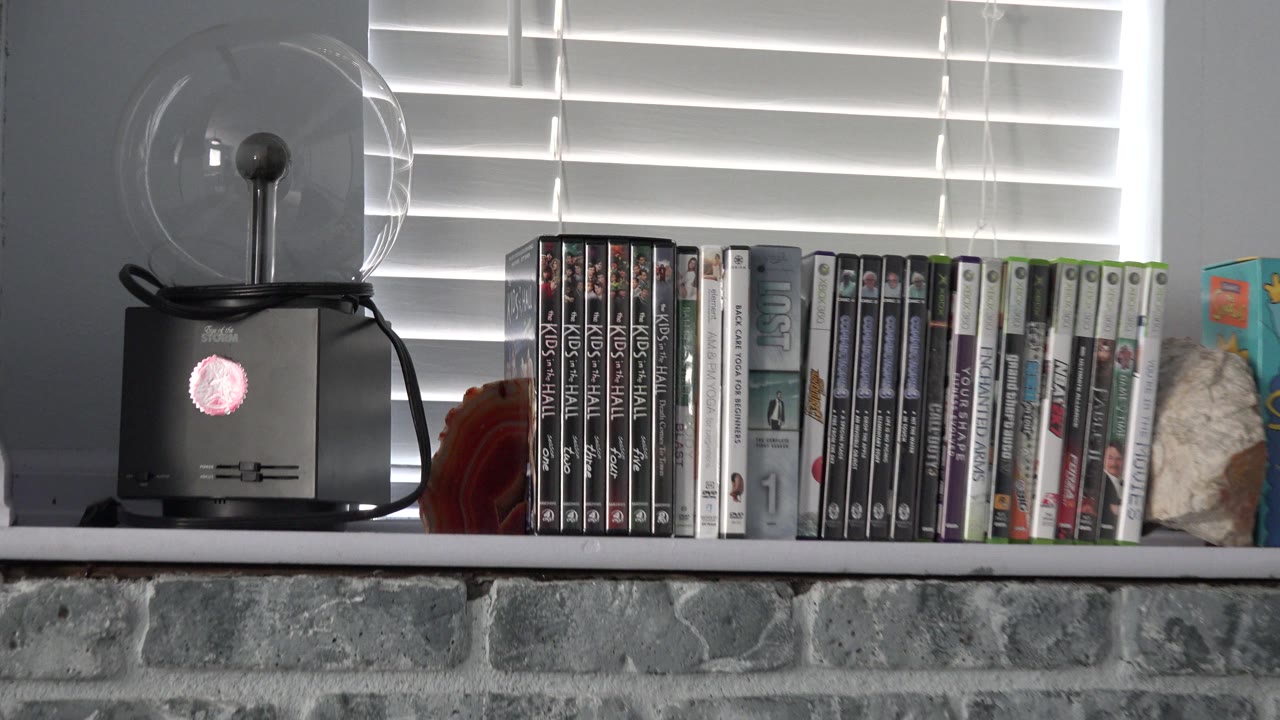 Westminster, Colorado interior frame holding on the video game cases and small fan near white blinds, with gray stonework below and no visible people.