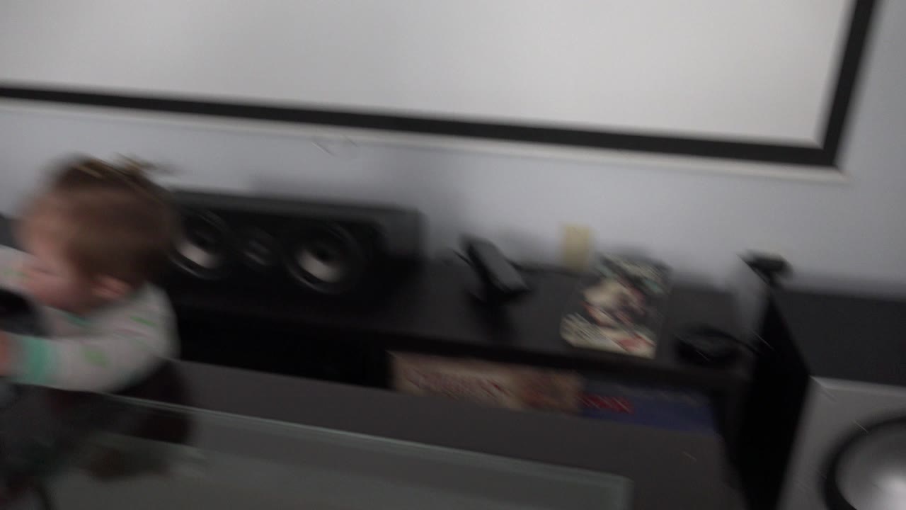 A blurred child passes at the left edge of a Westminster, Colorado home interior while a black entertainment center with speakers and board game boxes fills the frame.