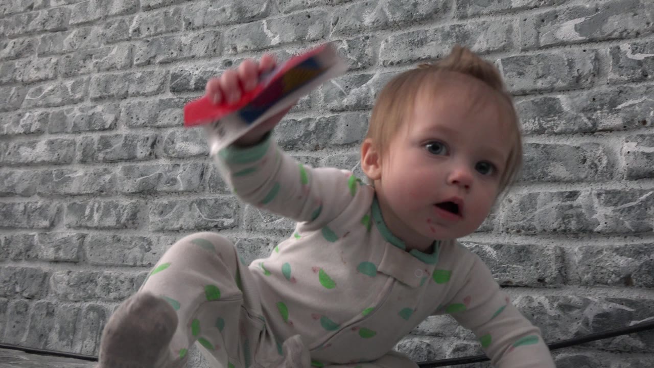A close low-angle view shows the baby facing forward in Westminster, Colorado with a red object raised beside the gray wall.