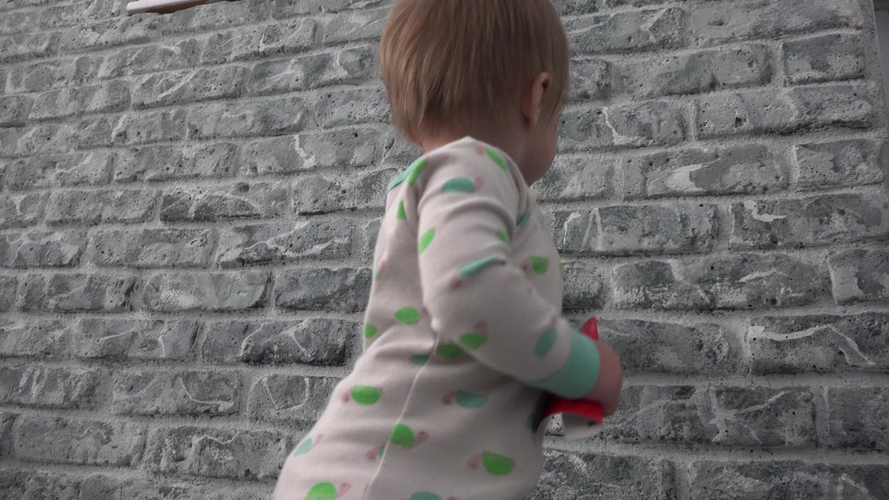 Toddler beside a grey brick wall with the back and side of the head visible.