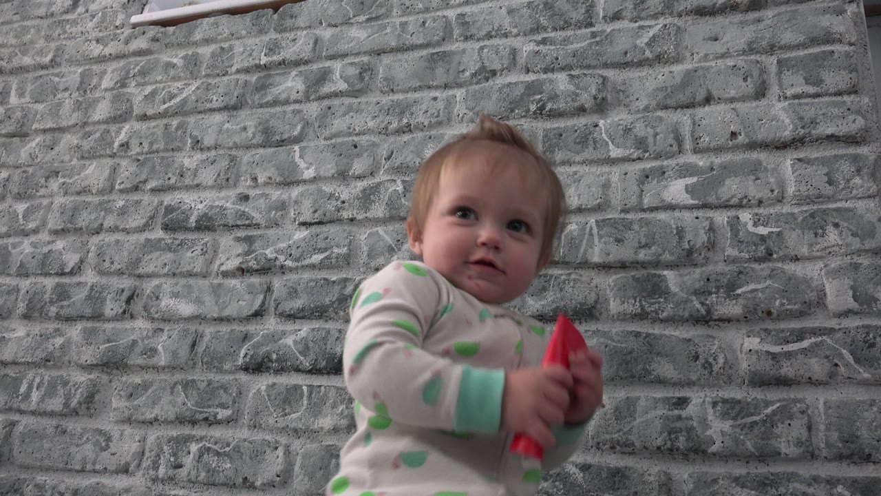 The baby looks slightly upward while gripping the red card, with the gray brick wall filling the Westminster, Colorado background.