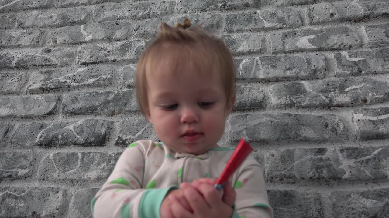 Baby looks at a red paper object held sideways in both hands.