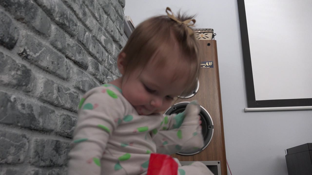 The child remains seated low in the Westminster, Colorado room, leaning forward with the red item partly visible at the bottom of the frame and a speaker behind them.