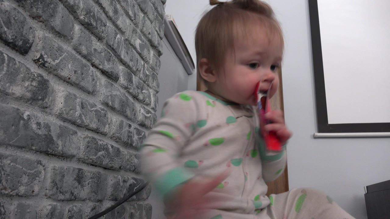 Baby chewing a red and blue piece of paper beside a gray brick wall.