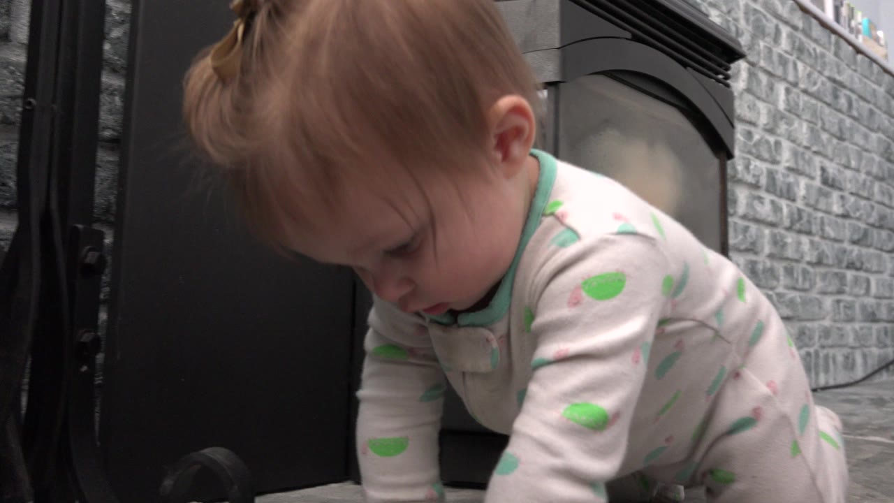 Baby in patterned pajamas crawling near a dark vertical surface and gray stone wall.