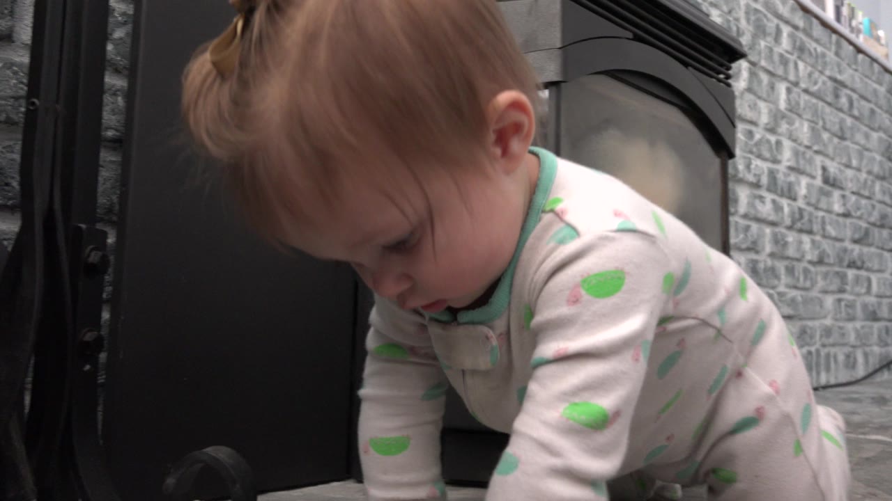 At 0:01, the baby remains low and forward in the frame, looking down while crawling beside the dark surface and gray stone background in Westminster, Colorado.