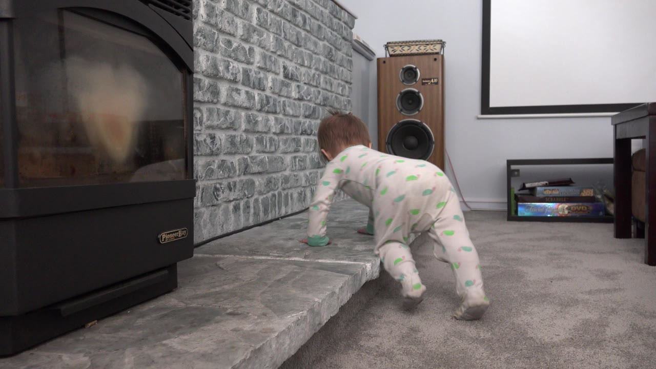 Small child crawling beside a raised stone fireplace hearth.