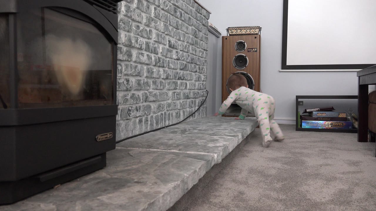 Baby crawls on carpet beside a stone fireplace ledge.