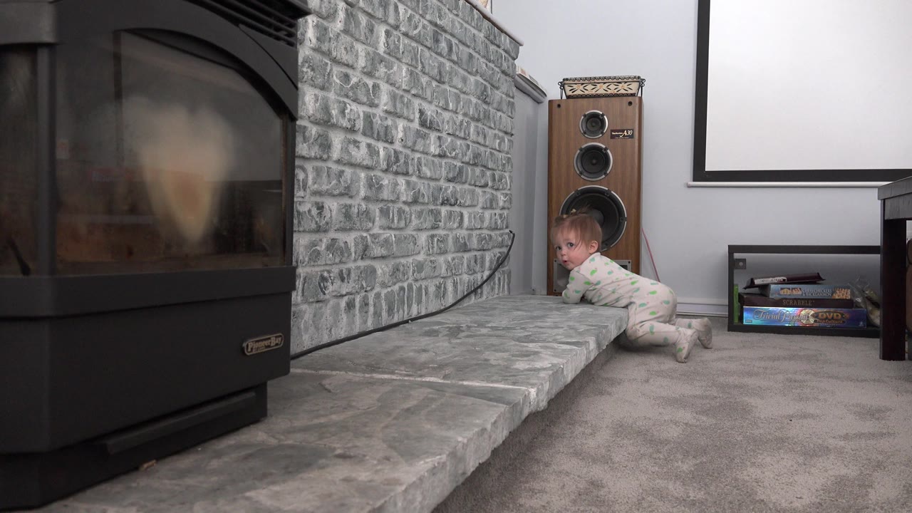 Toddler crawling beside a gray brick fireplace ledge and old speaker.