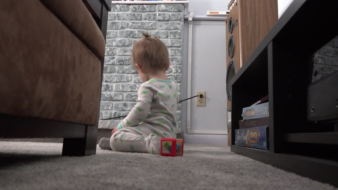 Baby sitting on carpet beside a red toy block in a living room.
