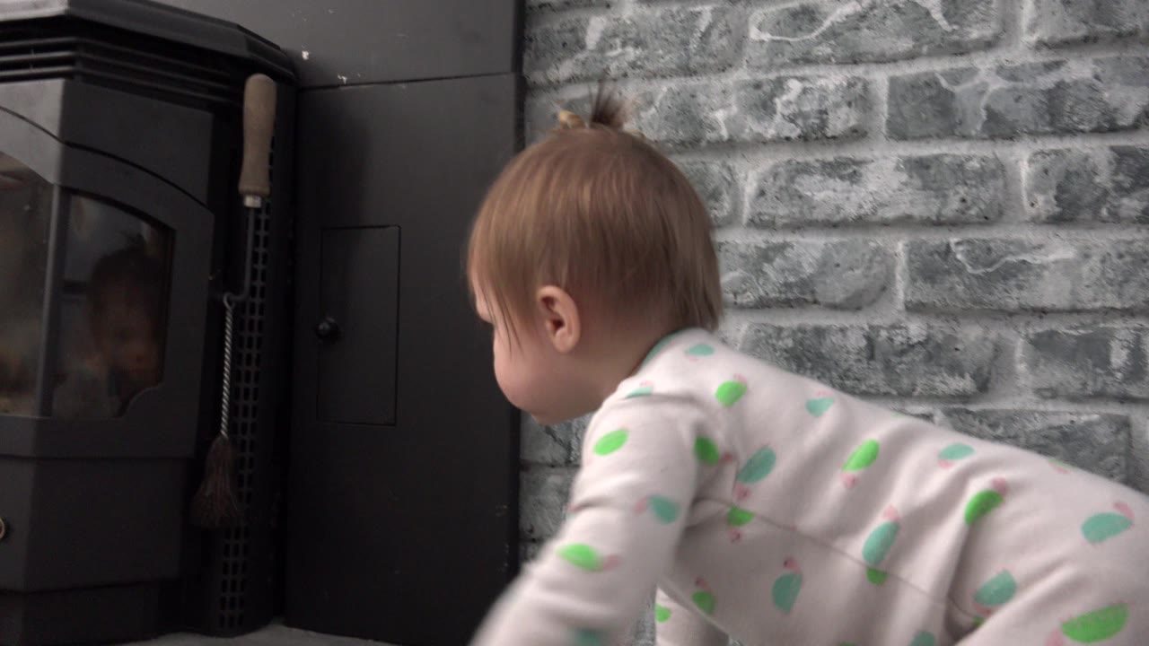 Baby crawling beside a black stove and gray brick wall.