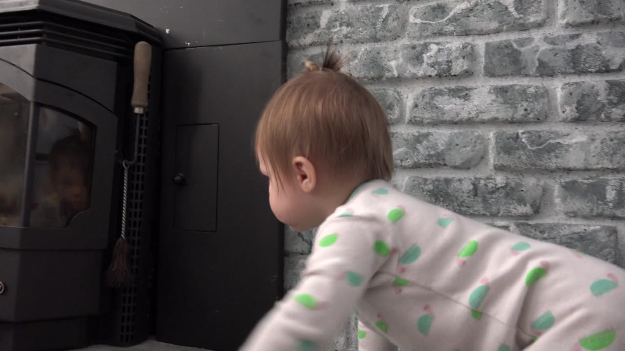 One second in, the baby continues crawling across the Westminster home interior, with the side of the black stove and textured gray brick wall filling the background.