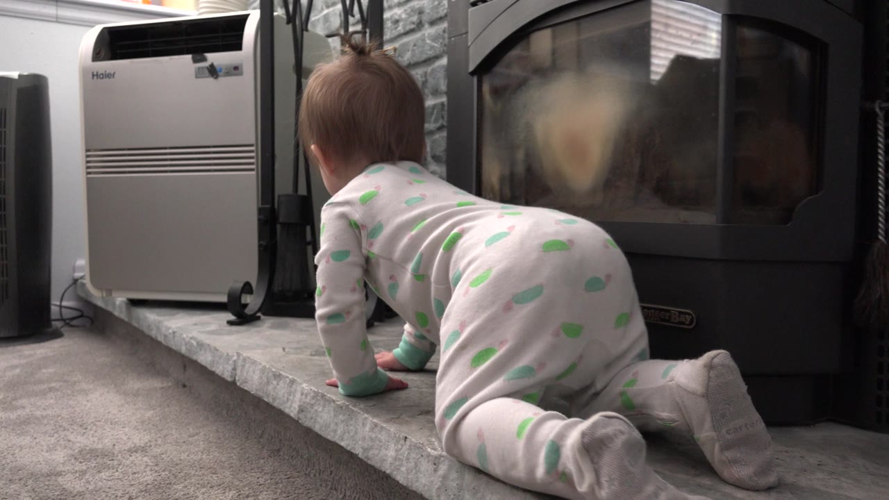Infant crawls on gray carpet toward a fireplace area.
