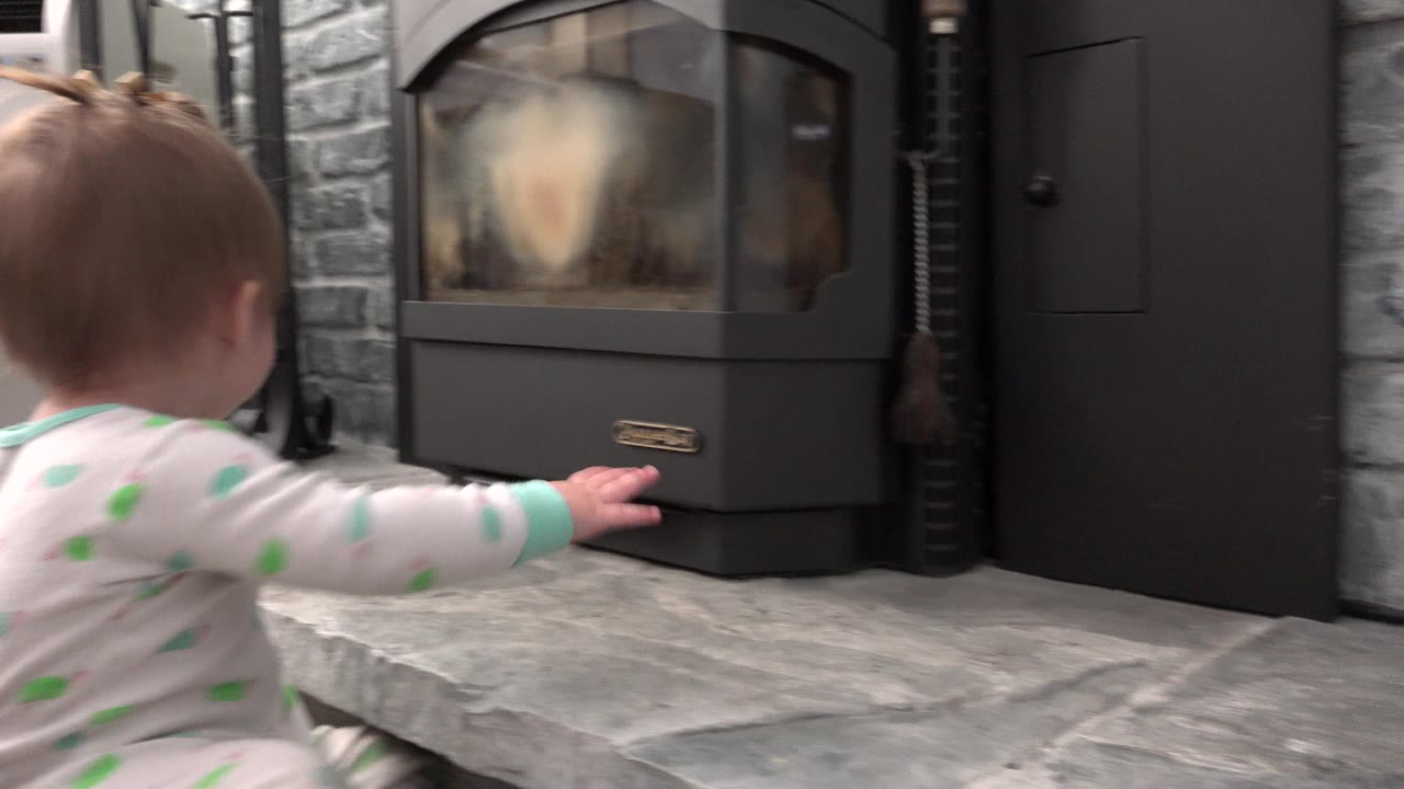 At 0:01 in Westminster, Colorado, the baby is closer to center frame with one arm extended toward the fireplace base on the raised gray hearth.