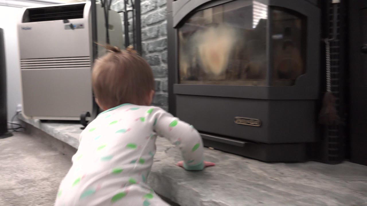 Baby crawls on the hearth near a fireplace and white appliance.