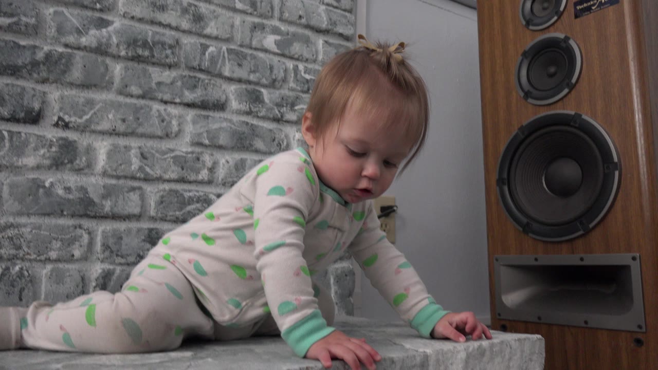 Young child crawling beside a wood speaker in a living room.