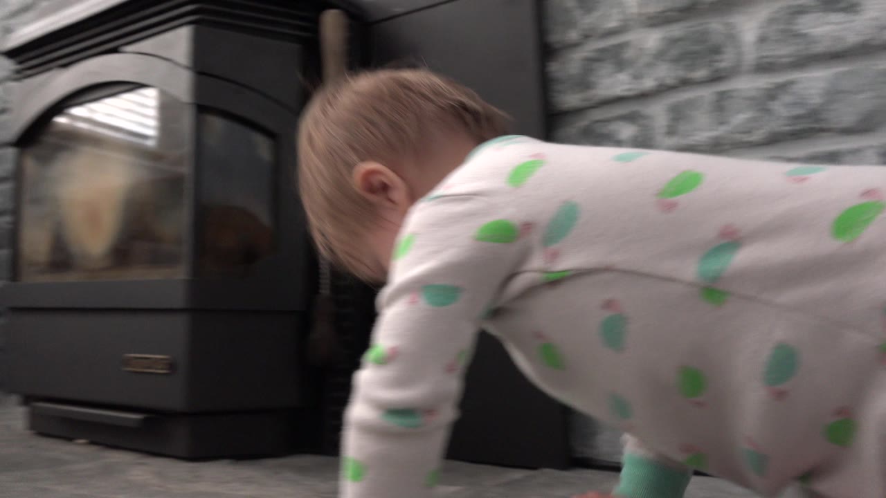 Baby crawling beside a black fireplace on a gray stone hearth.