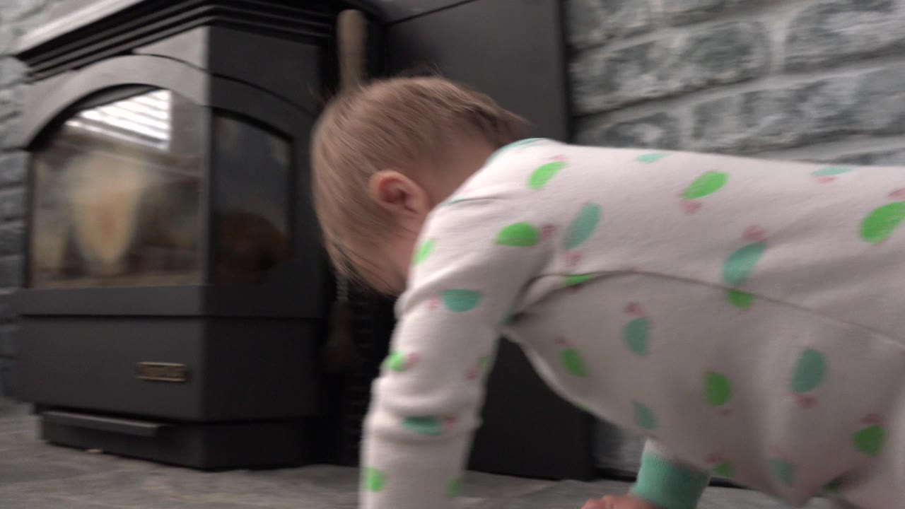 At 0:01 in Westminster, Colorado, the baby leans forward on hands with the black fireplace centered behind and gray stone surrounding the hearth.
