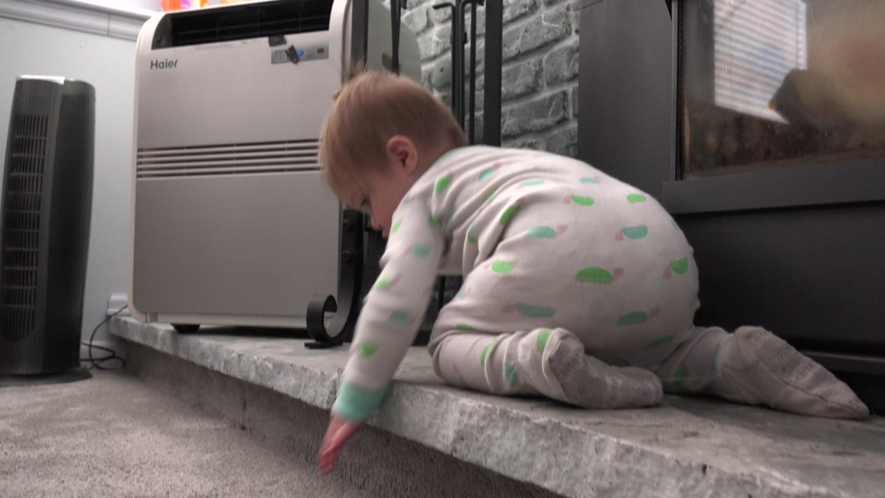 At 0:01 in Westminster, Colorado, the toddler stays on hands and knees on the stone ledge while reaching one hand toward the carpet below.