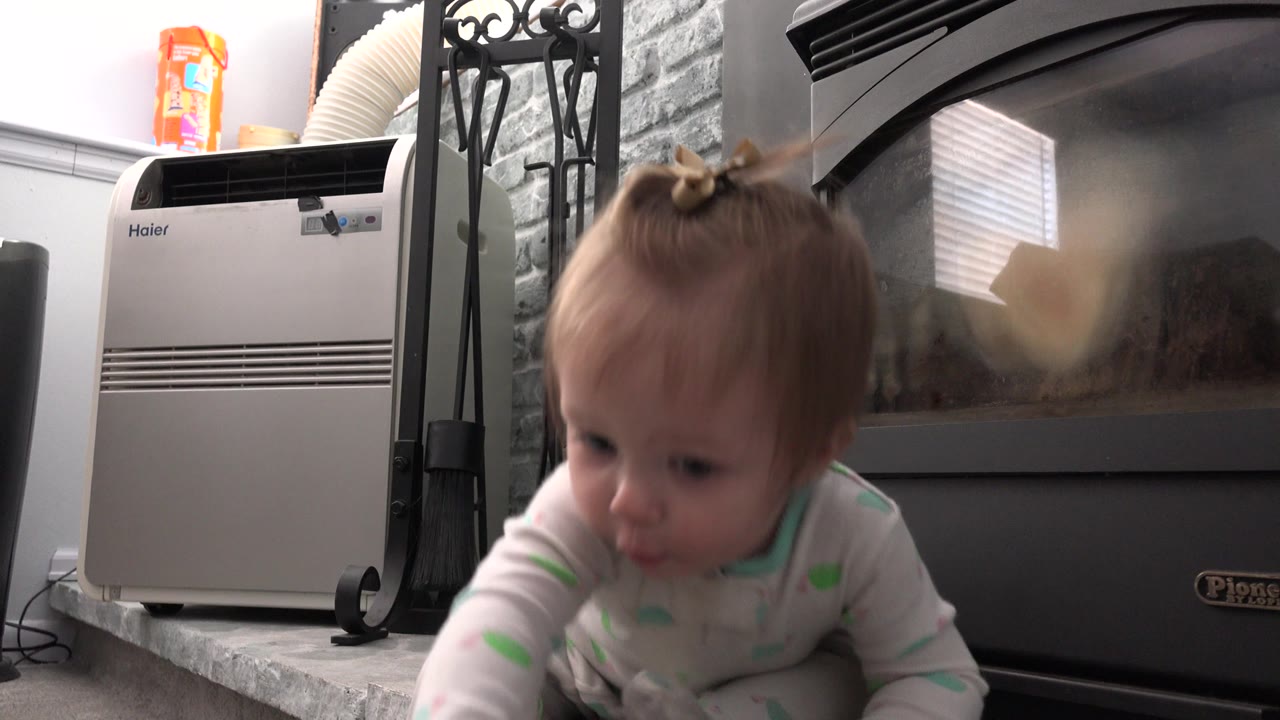 The baby moves closer to the low camera while the black stove or heater, white appliance, and stone hearth remain in the background of the Westminster, Colorado interior.
