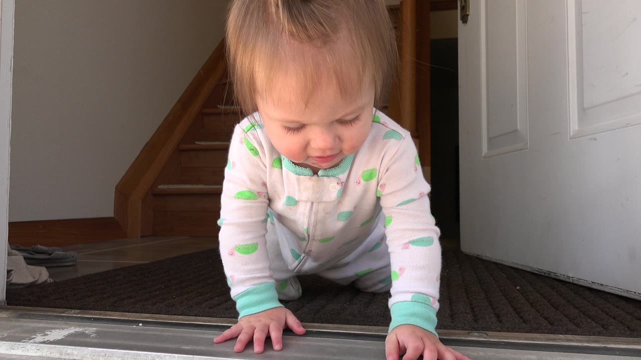 The baby remains on hands and knees near the doorway in Westminster, Colorado, looking down toward the carpet with the open white door filling the right side.
