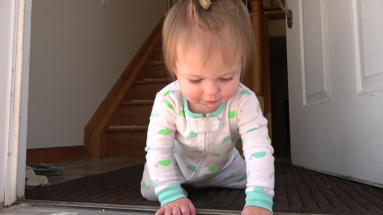 A baby crawls toward a low camera at an open doorway in Westminster, Colorado, with wood stairs and a white door behind.