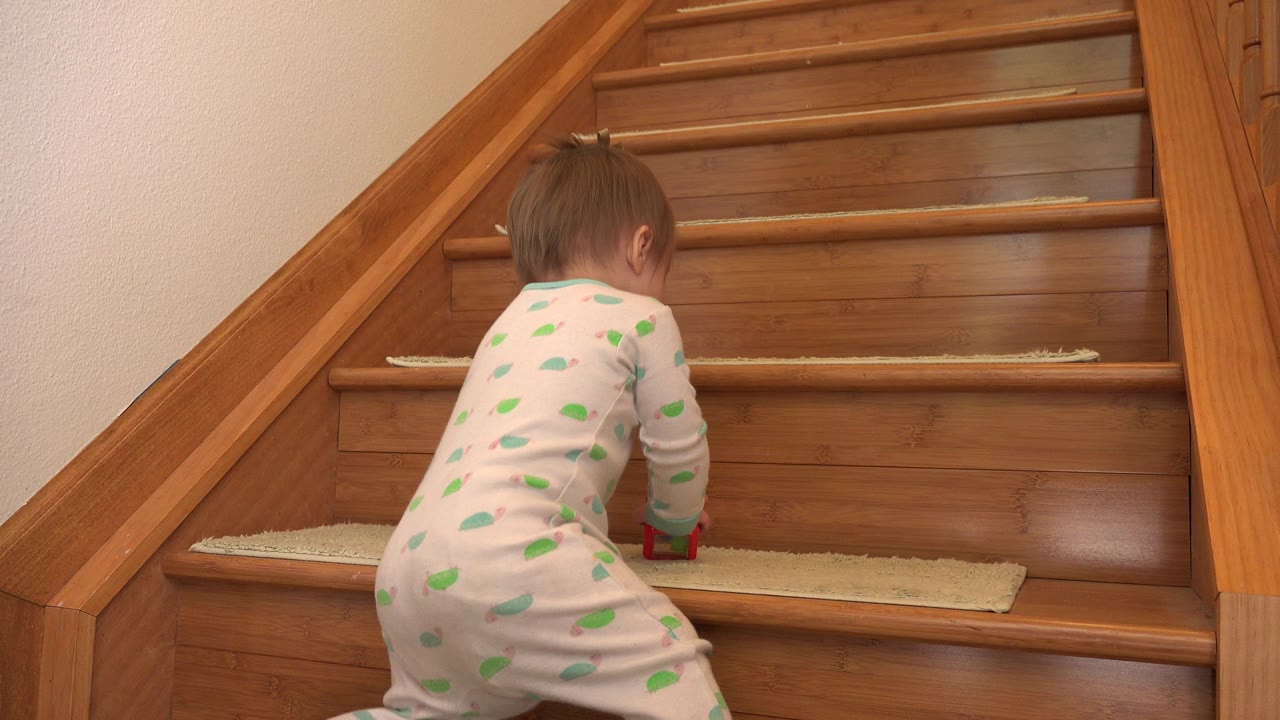 Baby in patterned pajamas climbing wooden stairs from behind.