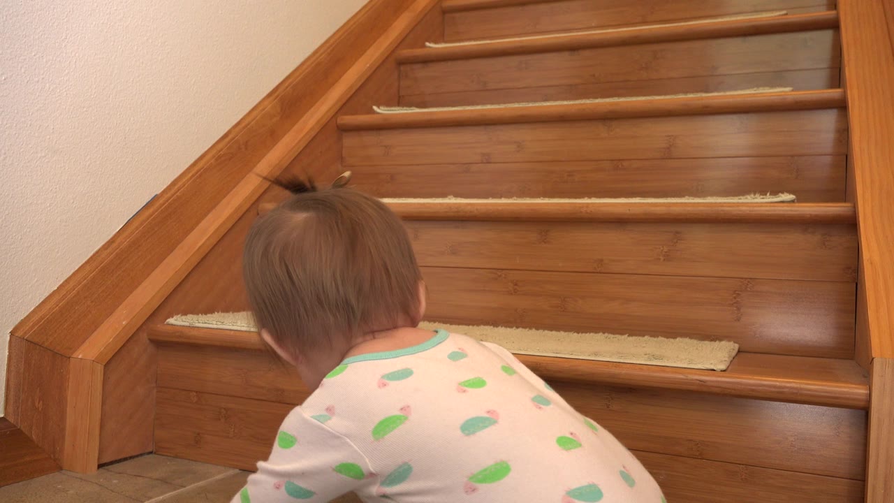 Toddler near the bottom of wooden stairs inside a home.