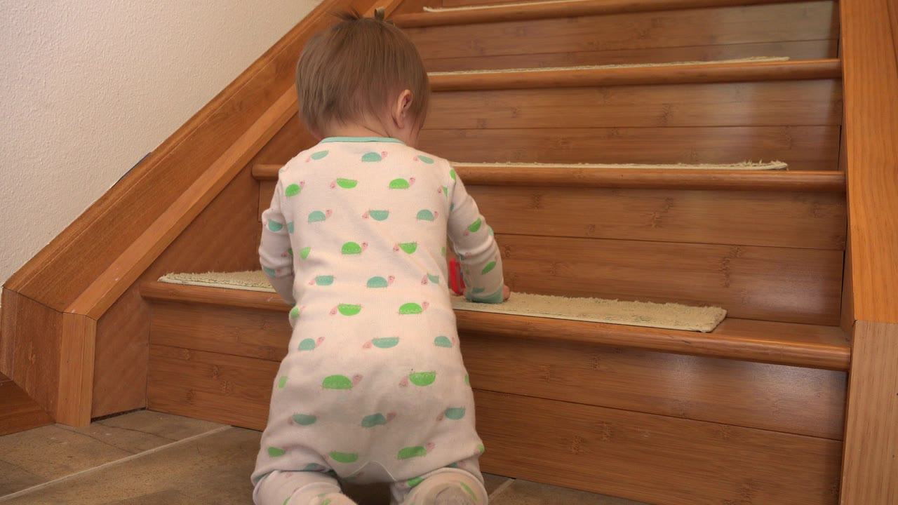 Baby in patterned pajamas facing wooden stairs.