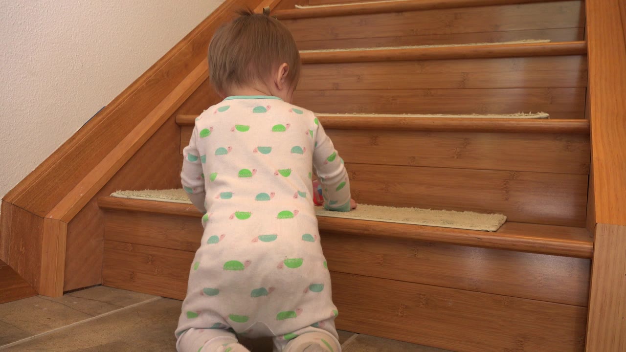 The baby leans forward toward the first wooden stair in the Westminster, Colorado interior, with the red toy partly visible near the hands.