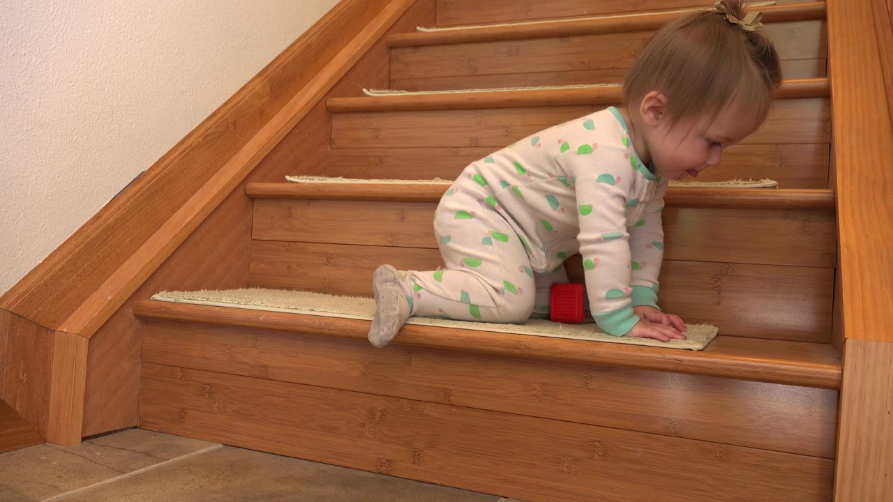 Baby kneeling on a stair beside a small red block.