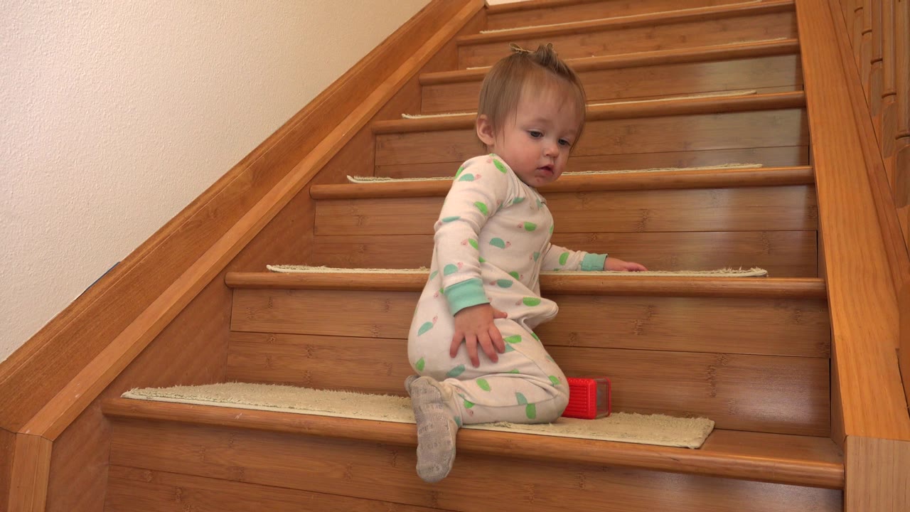 Baby sitting sideways on wooden stairs beside a red block.